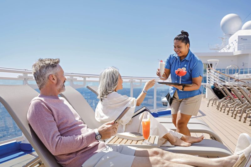 Guests receiving cocktails from crew member on top deck of cruise ship