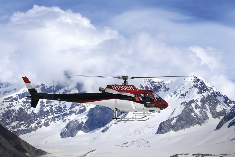 Red helicopter flying over mountains and glaciers