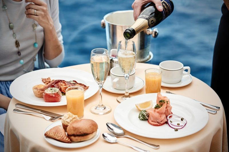 Two people dining on a balcony with a server pouring champagne