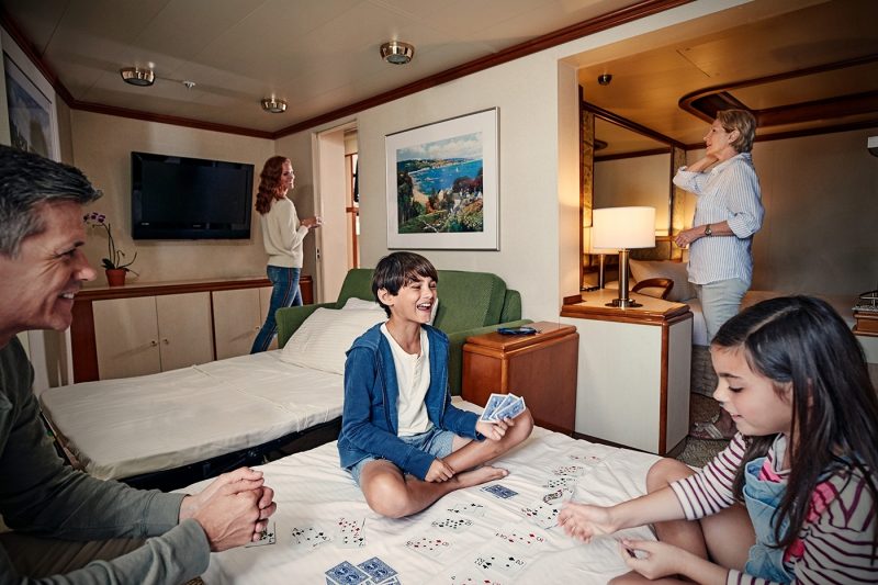 Family playing cards on a bed in a stateroom