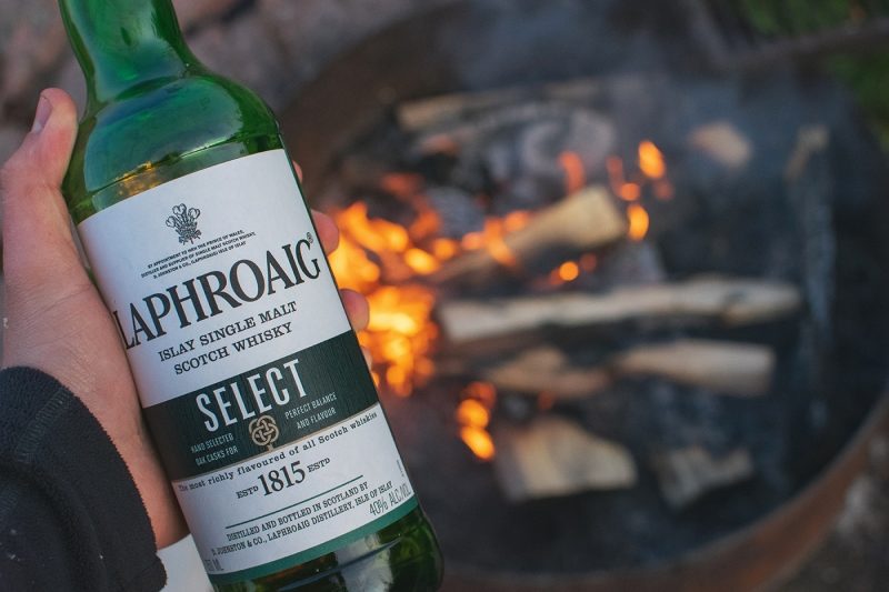 Man holding a bottle of Laphroaig whisky by a fire