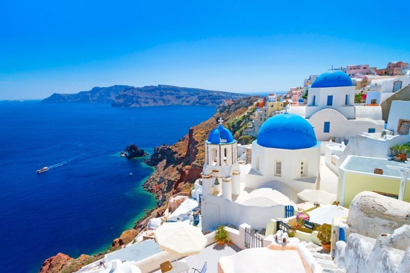 A view over blue seas with typical church buildings in the foreground in Santorini