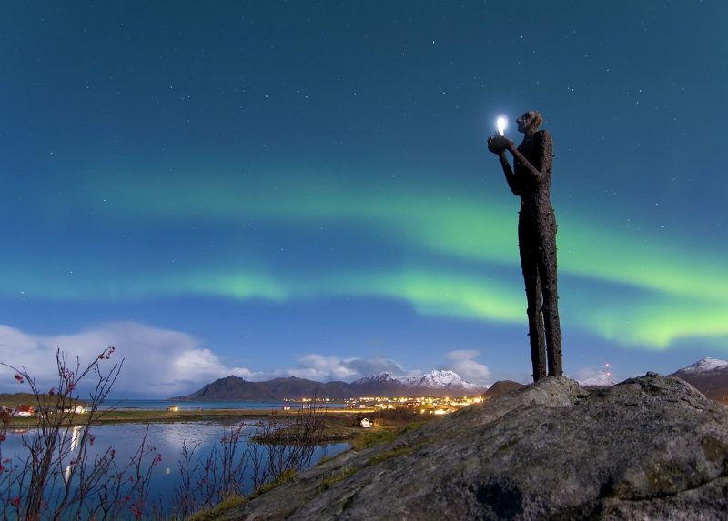 An outdoor sculpture holding a light, with northern lights in background