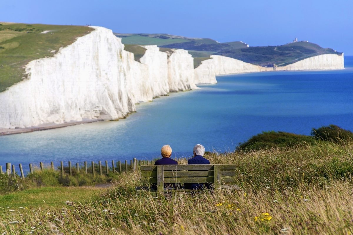 Two people sat on beach looking at white cliffs